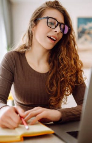 Beautiful businesswoman using a laptop wearing glasses while sitting at her workplace at home. Young woman working at home with a laptop. Concept of remote work, freelancing.